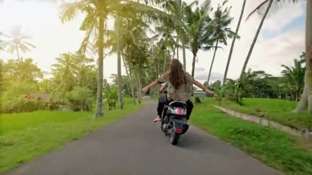 Pareja feliz tropezando en motocicleta en carretera tropical al atardecer. Foto al aire libre de una joven pareja montando en moto. Hombre montando en una motocicleta con su novia en el camino rural . — Vídeos de Stock