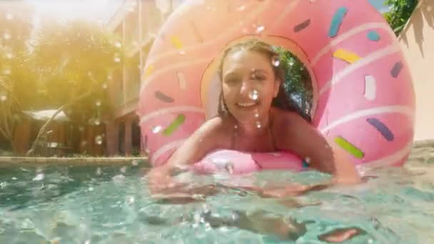 Napszemüveg, kék bikini fekve felfújható rózsaszín fánk úszó medence a nyári nap nő. Nézd meg kamera. Nő bikini medence görögdinnye gumi gyűrű pihentető nyaralás — Stock videók