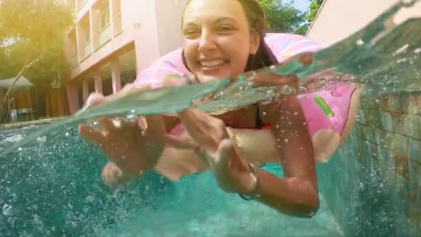 Young hipster millennial girl in sprinkled donut float at pool, smiling look at camera. Young happy woman relaxing on inflatable pool toy in blue swimming pool on sunny day. — Stock Video