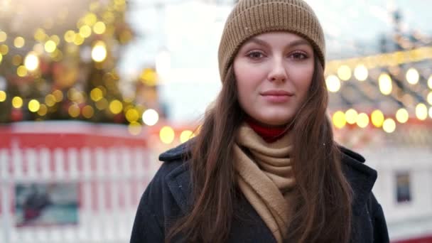Krásná žena stojí na náměstí ve městě mezi vánočními dekoracemi a dívá se přímo do kamery — Stock video