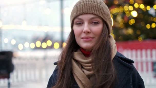 Όμορφη γυναίκα στέκεται στην πλατεία της πόλης ανάμεσα στα χριστουγεννιάτικα στολίδια και κοιτάζει κατευθείαν στην κάμερα — Αρχείο Βίντεο