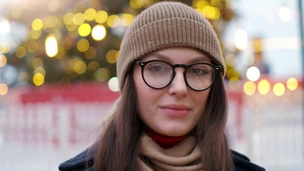 Pretty woman stands on the city square among Christmas decorations and looks straight into the camera — Stock Video