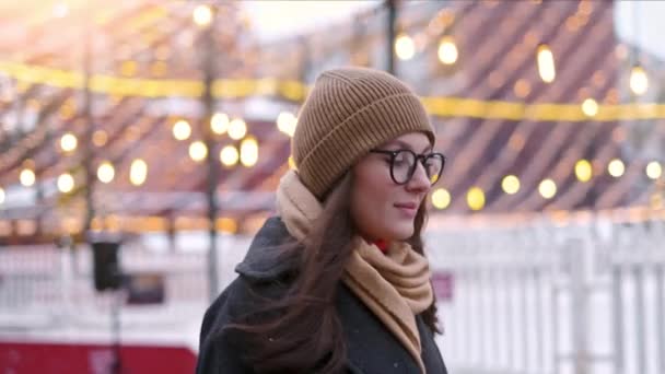 Mooie vrouw staat op het stadsplein onder kerstversiering en kijkt recht in de camera — Stockvideo