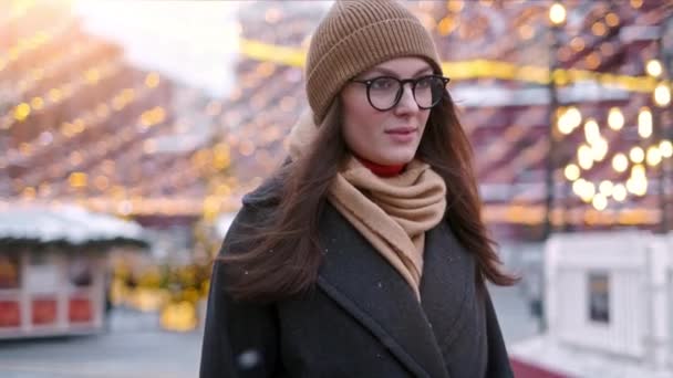 Mooie vrouw staat op het stadsplein onder kerstversiering en kijkt recht in de camera — Stockvideo