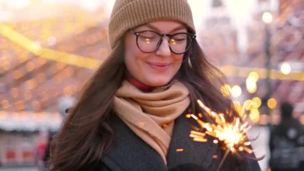 户外年轻美丽快乐微笑的女孩抱着火花，走在大街上。模特抬头，穿着时髦的冬装. — 图库视频影像