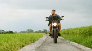 Motosiklet sürücüsü pirinç tarlalarına biniyor. Açık çekim, kırsal manzara. Seyahat ve spor fotoğrafçılığı. Hız ve özgürlük kavramı.