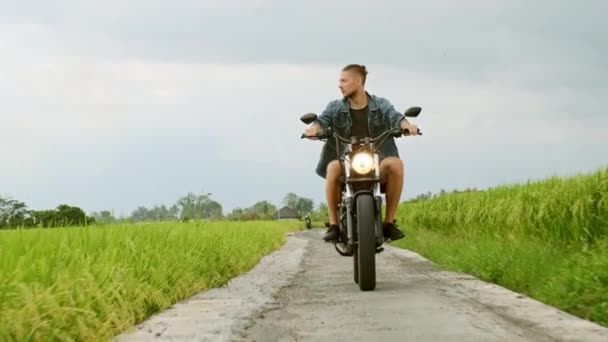 Motorista de moto montando em um os campos de arroz. Tiro ao ar livre, paisagem rural. Viagens e fotografia desportiva. Conceito de velocidade e liberdade . — Vídeo de Stock