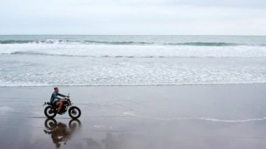 Sahilde motosiklet süren adam. Bali plaj günbatımı üzerinde vintage motosiklet. Genç hipster erkek özgürlük ve aktif yaşam tarzı zevk, bir bisikletçiler tur eğlenmek