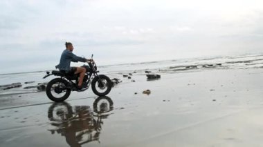 Sahilde motosiklet süren adam. Bali plaj günbatımı üzerinde vintage motosiklet. Genç hipster erkek özgürlük ve aktif yaşam tarzı zevk, bir bisikletçiler tur eğlenmek