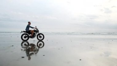 Sahilde motosiklet süren adam. Bali plaj günbatımı üzerinde vintage motosiklet. Genç hipster erkek özgürlük ve aktif yaşam tarzı zevk, bir bisikletçiler tur eğlenmek