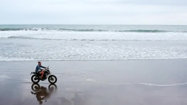 Sahilde motosiklet süren adam. Bali plaj günbatımı üzerinde vintage motosiklet. Genç hipster erkek özgürlük ve aktif yaşam tarzı zevk, bir bisikletçiler tur eğlenmek — Stok video