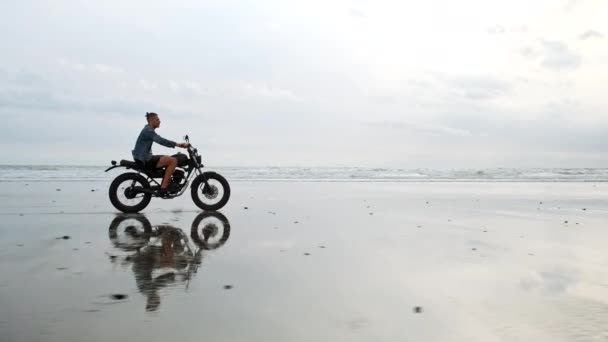 Mann mit Motorrad am Strand. Oldtimer Motorrad am Strand Sonnenuntergang auf Bali. Junge Hipster-Männchen genießen Freiheit und aktiven Lebensstil und haben Spaß auf einer Radtour — Stockvideo