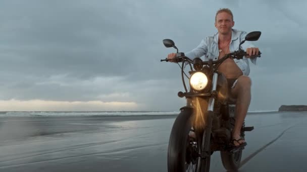 Hombre en moto a caballo en la playa. moto de época en la playa puesta de sol en Bali. Joven hipster masculino disfrutando de libertad y estilo de vida activo, divirtiéndose en un tour de ciclistas — Vídeo de stock