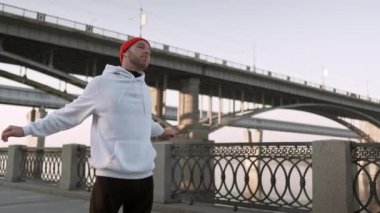 Genç adam koşmadan önce köprünün altında kolunu kaslarını geriyor. Yakışıklı atlet erkek germe egzersiz yapıyor, egzersiz için hazırlanıyor. Fitness konsepti.