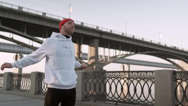 Junger Mann dehnt seine Armmuskeln unter der Brücke, bevor er läuft. gutaussehender Athlet, der Stretching-Übungen macht und sich auf das Training vorbereitet. Fitnesskonzept. — Stockvideo