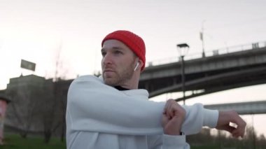 Temiz havada egzersiz yapmak. Kendinden emin genç adam açık havada dururken koşmadan önce vücudunu germe