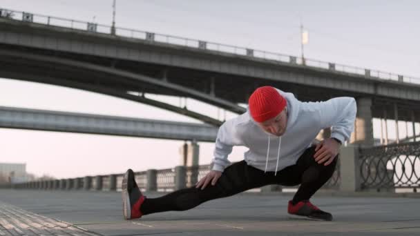 Genç adam koşmadan önce köprünün altında kolunu kaslarını geriyor. Yakışıklı atlet erkek germe egzersiz yapıyor, egzersiz için hazırlanıyor. Fitness konsepti. — Stok video