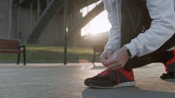 Joven atándose los cordones de los zapatos antes de comenzar el entrenamiento diario de rutina. Hombre haciendo ejercicios y calentamiento antes de correr y prueba de acondicionamiento físico en el puente . — Vídeos de Stock