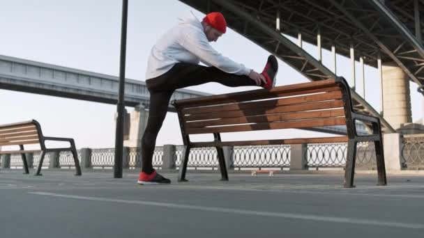 Strekkmann trener urban. Unge, fleksible hanner strekker seg dypt i byomgivelsene, i sakte bevegelse – stockvideo