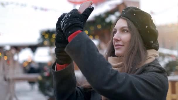 Mujer tomar fotos en la decoración del árbol de Navidad. Una hermosa joven mujer o niña haciendo selfie o usando el teléfono emocionalmente al aire libre frente a las decoraciones navideñas . — Vídeos de Stock