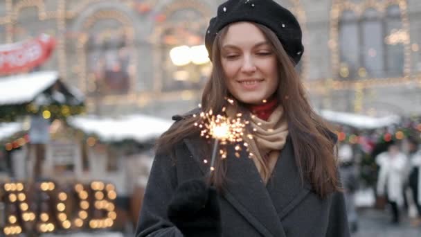 休日、クリスマス、人々のコンセプト - クリスマス市内中心部の背景の上にベンガル光を保持サンタスーツを着て若い幸せな女性 — ストック動画