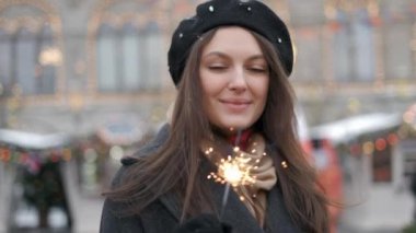 Açık genç güzel mutlu gülümseyen kız kıvılcım tutan, sokakta yürüyüş. Model yukarı bakıyor, şık kışlık kıyafetler giyiyor. Bel yukarı. Noel, Yeni Yıl, konsept. Sihirli kar yağışı. Tonda