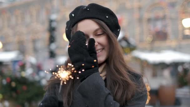 Glad ung kvinna som håller tomtebloss i handen utomhus. Detalj av flickan firar nyårsafton med Bengal ljus. Närbild av vacker kvinna som håller en gnistrande pinne på bokeh Cities Centre — Stockvideo