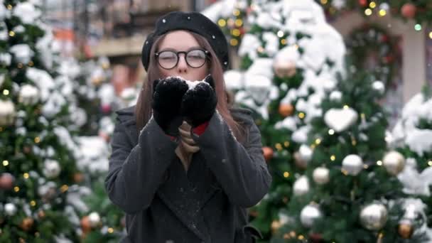 市内中心部で雪を吹く美冬の女の子。屋外。フライング・スノーフレーク楽しい若い女性を楽しんでいます。冬とクリスマスの時間のコンセプト — ストック動画