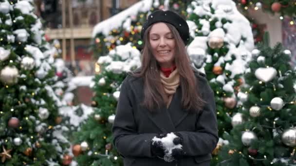 LOW MOTION: Jovem mulher soprando neve. Jovem mulher a soprar neve. Retrato de mulher jovem bonito soprando na neve em suas mãos. Neve dispersa em direções diferentes — Vídeo de Stock