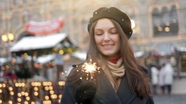 Jovem alegre segurando sparklers na mão ao ar livre. Detalhe da menina celebrando véspera de ano novo com luz bengala. Close-up de mulher bonita segurando uma vara espumante no centro de cidades de bokeh — Vídeo de Stock