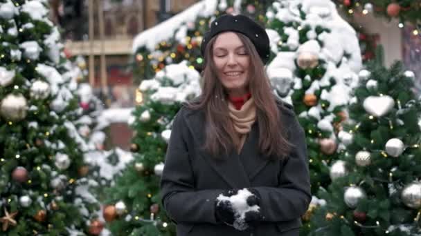 Belleza Chica de invierno Soplando nieve en el centro de la ciudad. Al aire libre. Copos de nieve voladores. Joven alegre divirtiéndose. Concepto de invierno y Navidad — Vídeo de stock