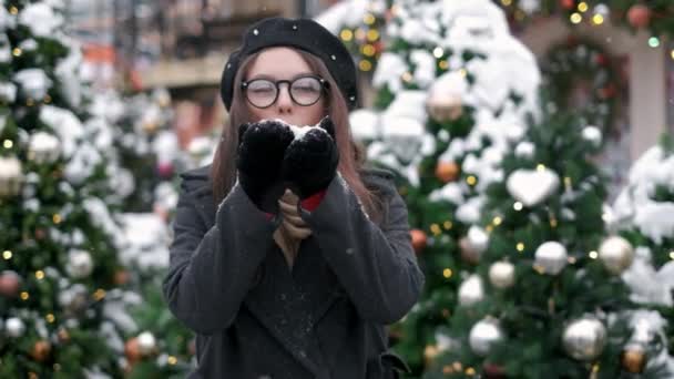 スローモーション:雪を吹く若い女性。雪を吹く若い女性彼女の手の中で雪に吹くかわいい若い女性の肖像画。雪が異なる方向に散乱 — ストック動画