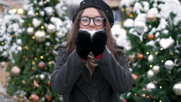 Slow Motion: jonge vrouw waait sneeuw. Jonge vrouw waait sneeuw. Portret van schattige jonge vrouw waait op sneeuw in haar handen. Sneeuw verstrooit in verschillende richtingen — Stockvideo