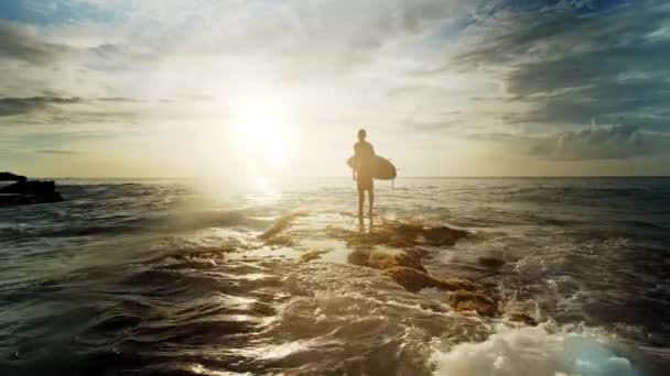 Een man staat met een surf in zijn handen op de kust. — Stockvideo