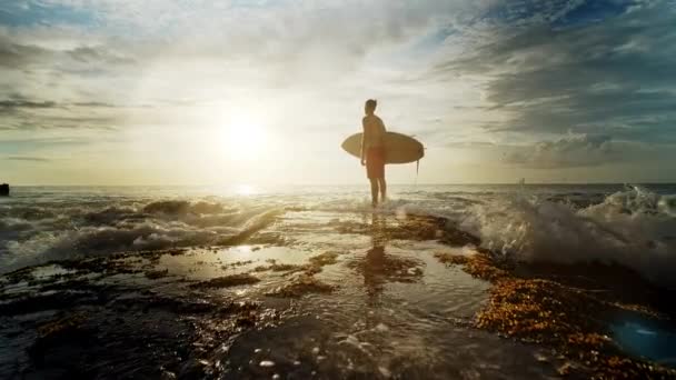 Мужчина стоит с серфингом в руках на берегу моря . — стоковое видео