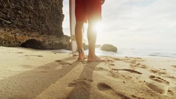 Um homem está de pé com um surfe em suas mãos na costa do mar . — Vídeo de Stock