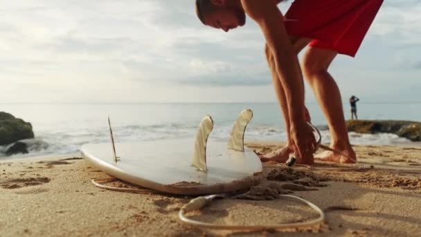 Een man staat met een surf in zijn handen op de kust. — Stockvideo