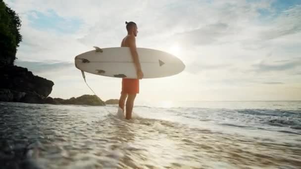 Un homme se tient debout avec un surf dans ses mains sur le bord de la mer . — Video