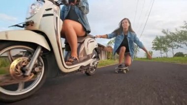 Bir grup arkadaş pateni ve motosiklet. Neşeli gençler dışarıda eğleniyor. Güneşli bir günde iki kadın biniyor. Mutlu genç çift yolda kaykay ile eğleniyor.