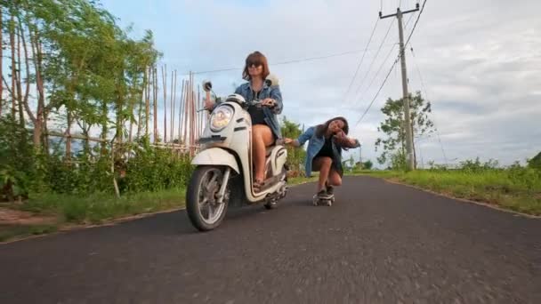 Grupo de amigos patinaje y motociclismo. Adolescentes alegres divirtiéndose al aire libre. Dos mujeres montando en un día soleado. Feliz joven pareja divirtiéndose con el monopatín en el camino . — Vídeo de stock