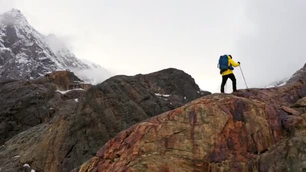 Jonge man gele jas wandelen omhoog berghelling backpacken winter wandeling extreme omstandigheden Zwitserse Alpen Aerial drone vlucht beelden — Stockvideo