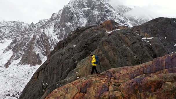 Jonge man gele jas wandelen omhoog berghelling backpacken winter wandeling extreme omstandigheden Zwitserse Alpen Aerial drone vlucht beelden — Stockvideo