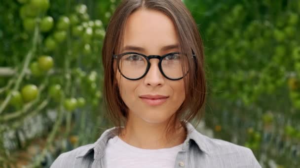 Retrato de menina bonita em chapéu e avental em pé em estufa sorrindo e olhando para a câmera. Agricultura moderna, juventude feliz e conceito de profissão . — Vídeo de Stock