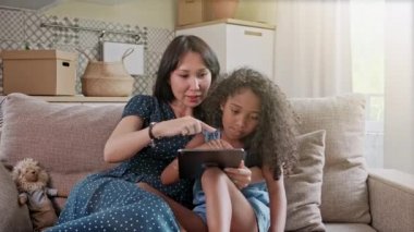 Anne ve Kızı bir ev iç bir dijital tablet te eğleniyor. Oturma odasında evde bir dijital tablet kullanarak sevimli mutlu anne ve kızı.