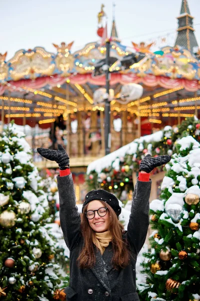 Mädchen spielt mit Schnee im Park. junges Mädchen wirft Schnee, eine schöne Kirmes mit Lichtern und Glühbirnen, geschmückte Weihnachtsbäume — Stockfoto
