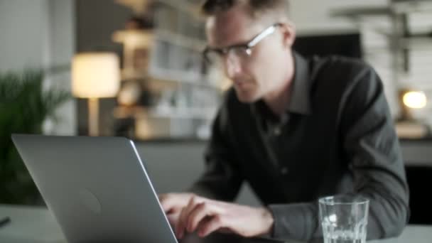 Молодой человек фрилансер с помощью ноутбука онлайн работает из офиса в Интернете, улыбаясь сосредоточены Тысячелетний парень печатают на компьютере серфинга веб-глядя на экран наслаждаясь отдаленной работы — стоковое видео