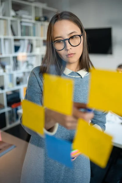 Young Business Woman Brainstorming. Asian Woman Writing Down Ideas On Sticky Notes Attached To Glass Wall (dalam bahasa Inggris). Konsep Sukses Bisnis — Stok Foto
