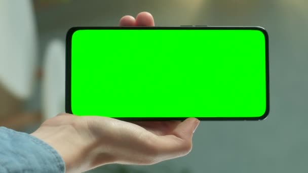 Junge Frau zu Hause hält Chroma Key Green Screen Smartphone Inhalte beobachten, ohne zu berühren oder zu wischen. Mädchen benutzen Handy, surfen im Internet. Mit vertikaler Bildschirmausrichtung 9: 16 — Stockvideo