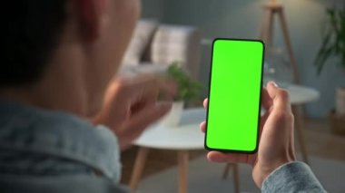 Green Mock-up Smartphone kullanarak Evdeki Genç Adam 'ın Bir Sandalyede Oturması. Çocuk 