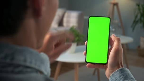 Vista posterior de un joven en casa sentado en una silla con un teléfono inteligente de pantalla falsa verde. Boy está viendo contenido sin tocar la pantalla del gadget. Modent Tecnología y Concepto de Información . — Vídeos de Stock